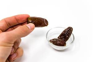 Hand holds fresh dates next to a tiny glas bowl with white background