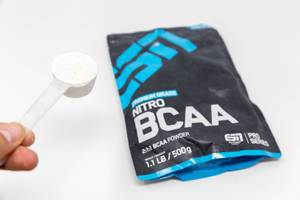 Hand holds little measuring spoon with ESN Nitro BCAA powder for athletes and a sporty lifestyle