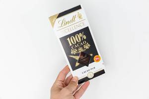 Hand holds the new Lindt Excellence chocolate bar with 100% pure cacao on a white background