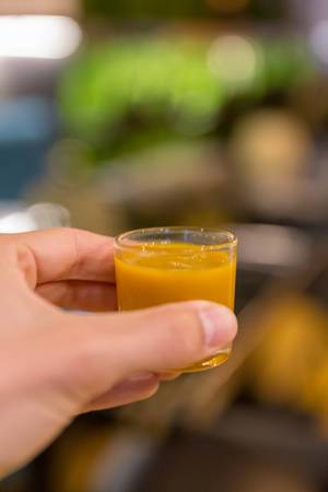 Hand holds tumeric-ginger shot for nightcap at Fit Kitchen Restaurant in Barcelona, Spain