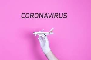 Hand in medical glove holding small airplane with Coronavirus text