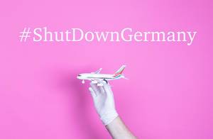 Hand in medical glove holding small airplane with #ShutDownGermany text.jpg