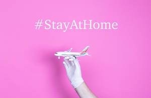 Hand in medical glove holding small airplane with #StayAtHome text.jpg