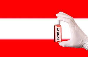 Hand in protective gloves holding COVID-19 test tube in front of flag of Austria