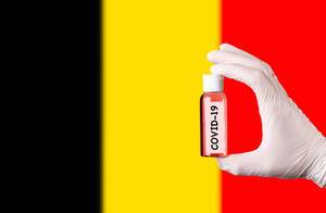 Hand in protective gloves holding COVID-19 test tube in front of flag of Belgium