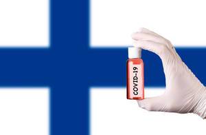 Hand in protective gloves holding COVID-19 test tube in front of flag of Finland