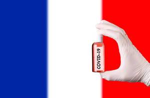 Hand in protective gloves holding COVID-19 test tube in front of flag of France