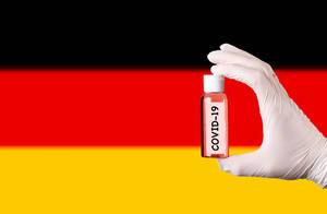 Hand in protective gloves holding COVID-19 test tube in front of flag of Germany