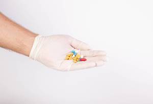 Hand mit Latexhandschuh  hält bunte Medikamente / Tabletten, vor weißem Hintergrund