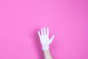 Hand mit medizinischem Handschuh vor pinkem Hintergrund