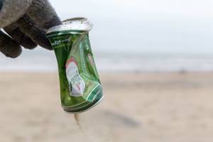 Hand picks up old beer can from the beach and reduces pollution