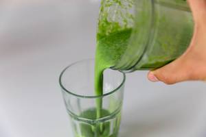 Hand pours a green spinach-almond power protein drink into a glass
