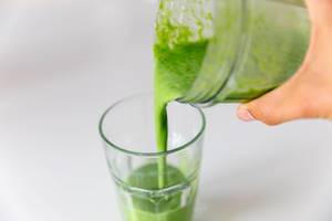 Hand schenkt ein grünes Mandel-Spinat-Getränk in ein Trinkglas