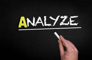 Hand schreibt das Wort "Analyze" - analysieren - mit Kreide auf eine schwarze Tafel