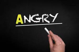 Hand schreibt das Wort "Angry" - wütend - mit Kreide auf eine schwarze Tafel