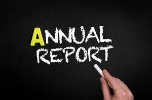 Hand schreibt das Wort "Annual Report" - Jahresbericht - mit Kreide auf eine schwarze Tafel