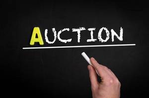 Hand schreibt das Wort "Auction" - Auktion / Versteigerung - mit Kreide auf eine schwarze Tafel