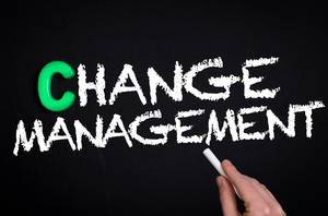 Hand schreibt das Wort "Change Management" - Änderungsmanagement / Führungswechsel - mit Kreide auf eine schwarze Tafel