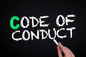 Hand schreibt das Wort "Code of Conduct" - Verhaltenskodes - mit Kreide auf eine schwarze Tafel