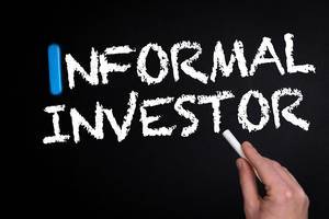 Hand schreibt das Wort "Informal Investor" - informeller Investor - mit Kreide auf eine schwarze Tafel