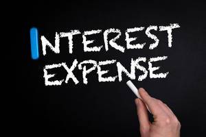 Hand schreibt das Wort "Interest Expense" - Zinsaufwand - mit Kreide auf eine schwarze Tafel