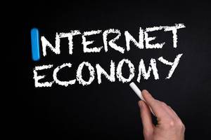 Hand schreibt das Wort "Internet Economy" - Internetwirtschaft - mit Kreide auf eine schwarze Tafel