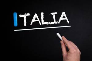 Hand schreibt das Wort "Italia" mit Kreide auf eine schwarze Tafel