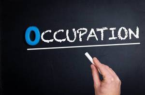 Hand schreibt das Wort "Occupation" - Beschäftigung / Beruf - mit Kreide auf eine schwarze Tafel