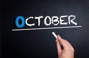 Hand schreibt das Wort "October" - Oktober - mit Kreide auf eine schwarze Tafel