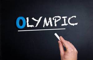 Hand schreibt das Wort "Olympic" - Olympisch - mit Kreide auf eine schwarze Tafel