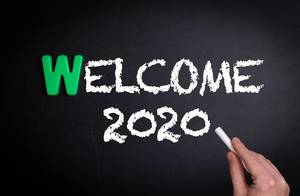 Hand schreibt das Wort "Welcome 2020" - Willkommen 2020 - mit Kreide auf eine schwarze Tafel