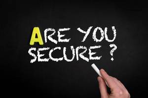 Hand schreibt  "Are you secure?" - Bist du abgesichert? - mit Kreide auf eine schwarze Tafel