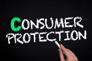 Hand schreibt "Consumer Protection" - Verbraucherschutz - mit Kreide auf eine schwarze Tafel