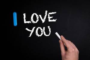 Hand schreibt "I love you" - Ich liebe dich - mit Kreide auf eine schwarze Tafel