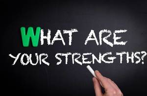 Hand schreibt "What are your strengths?" - was sind deine Stärken? - mit Kreide auf eine schwarze Tafel