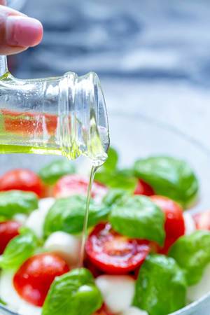 Hand schüttet frisches Olivenöl aus einer Karaffe auf den ausgewogenen Salat