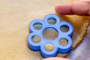Hand sticht Kekse aus dem Teig aus, mit Hilfe eines blauen Plätzchenförmchens in Blumenform