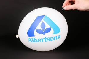 Hand uses a needle to burst a balloon with Albertsons logo