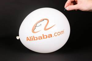 Hand uses a needle to burst a balloon with Alibaba logo