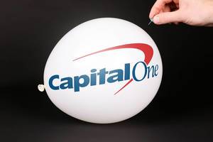 Hand uses a needle to burst a balloon with Capital One logo