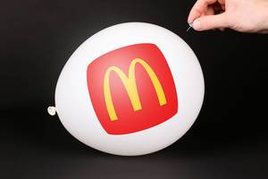 Hand uses a needle to burst a balloon with McDonald