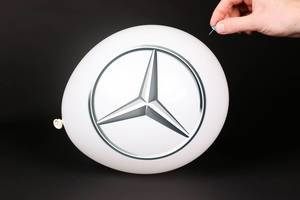 Hand uses a needle to burst a balloon with Mercedes Benz logo