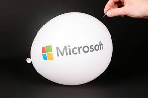 Hand uses a needle to burst a balloon with Microsoft logo