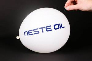 Hand uses a needle to burst a balloon with Neste Oil logo