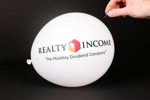 Hand uses a needle to burst a balloon with Realty Income logo