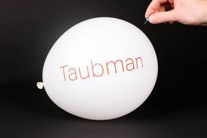 Hand uses a needle to burst a balloon with Taubman logo
