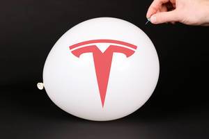 Hand uses a needle to burst a balloon with Tesla logo