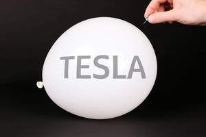 Hand uses a needle to burst a balloon with TESLA text