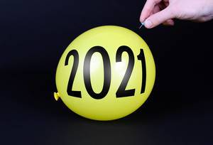 Hand uses a needle to burst a yellow balloon with 2021 text