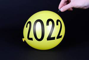 Hand uses a needle to burst a yellow balloon with 2022 text